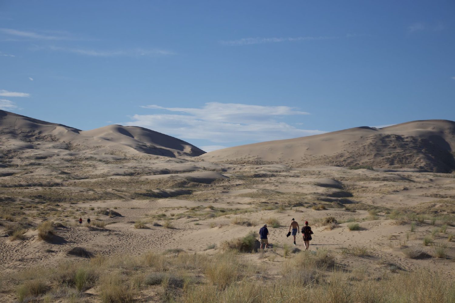 Small silhouettes of hikers walking across the desert floor toward the towering Kelso Sand Dunes