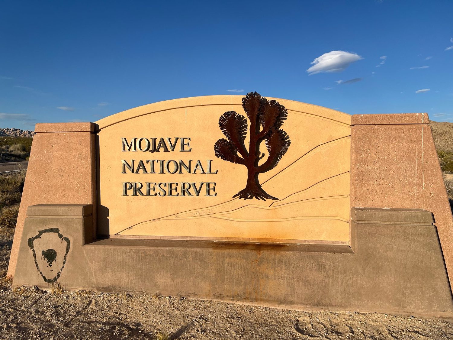 Brown National Park Service welcome sign reading Mojave National Preserve, set against a blue desert sky
